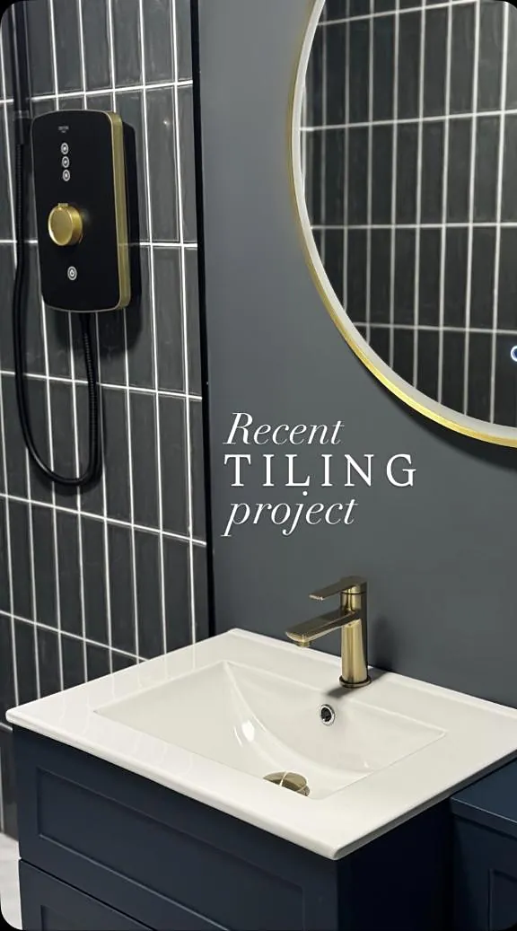 A navy bathroom vanity with brass tap and a round brass mirror over vertical tiles