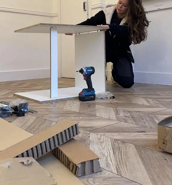 Emma assembling a kitchen unit on a herringbone floor